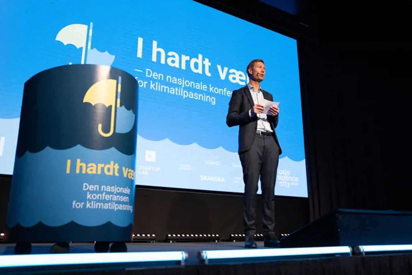 A man stands presenting on a stage that seems like a conference.