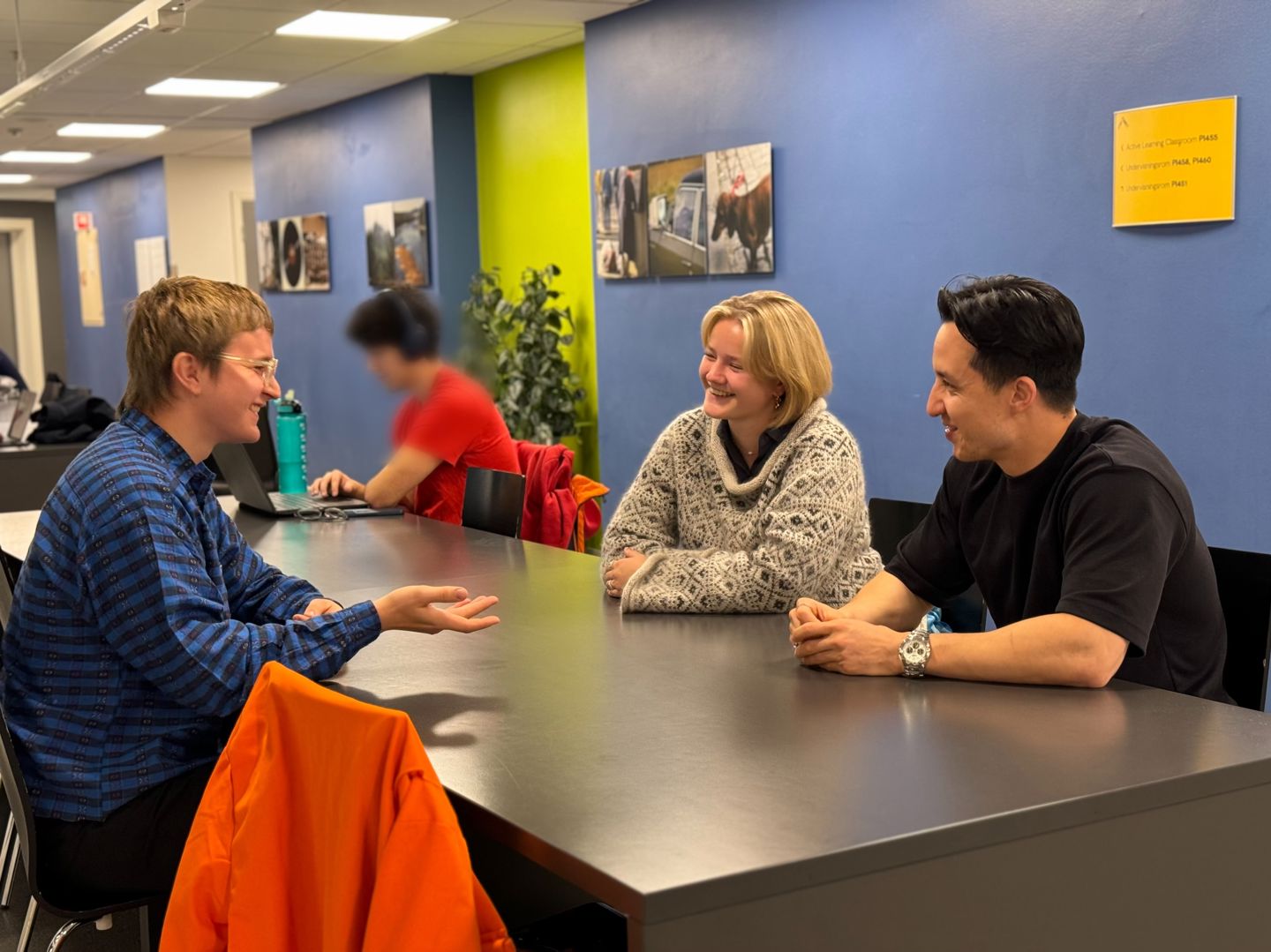 To gutter og en jente sitter rundt et bord og diskuterer.